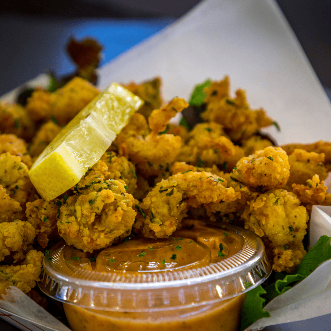 A close-up view of crispy fried calamari served in a casual container with a fresh lemon wedge and spicy remoulade sauce.